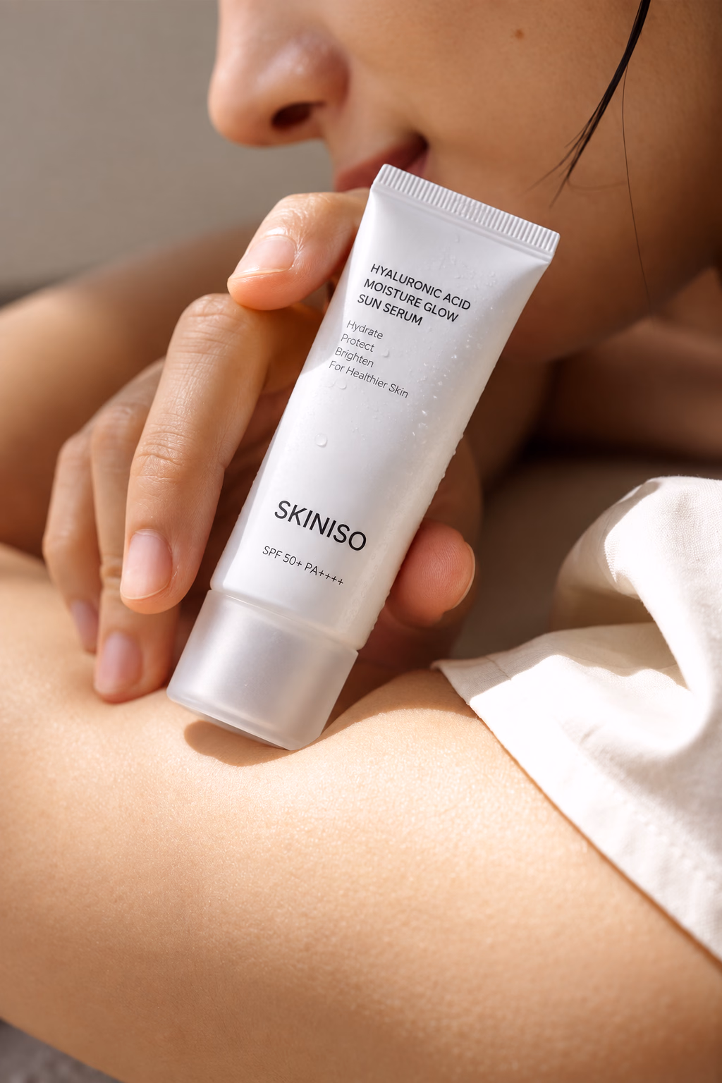 A hand holding a SkiniSo tube over a white sheet